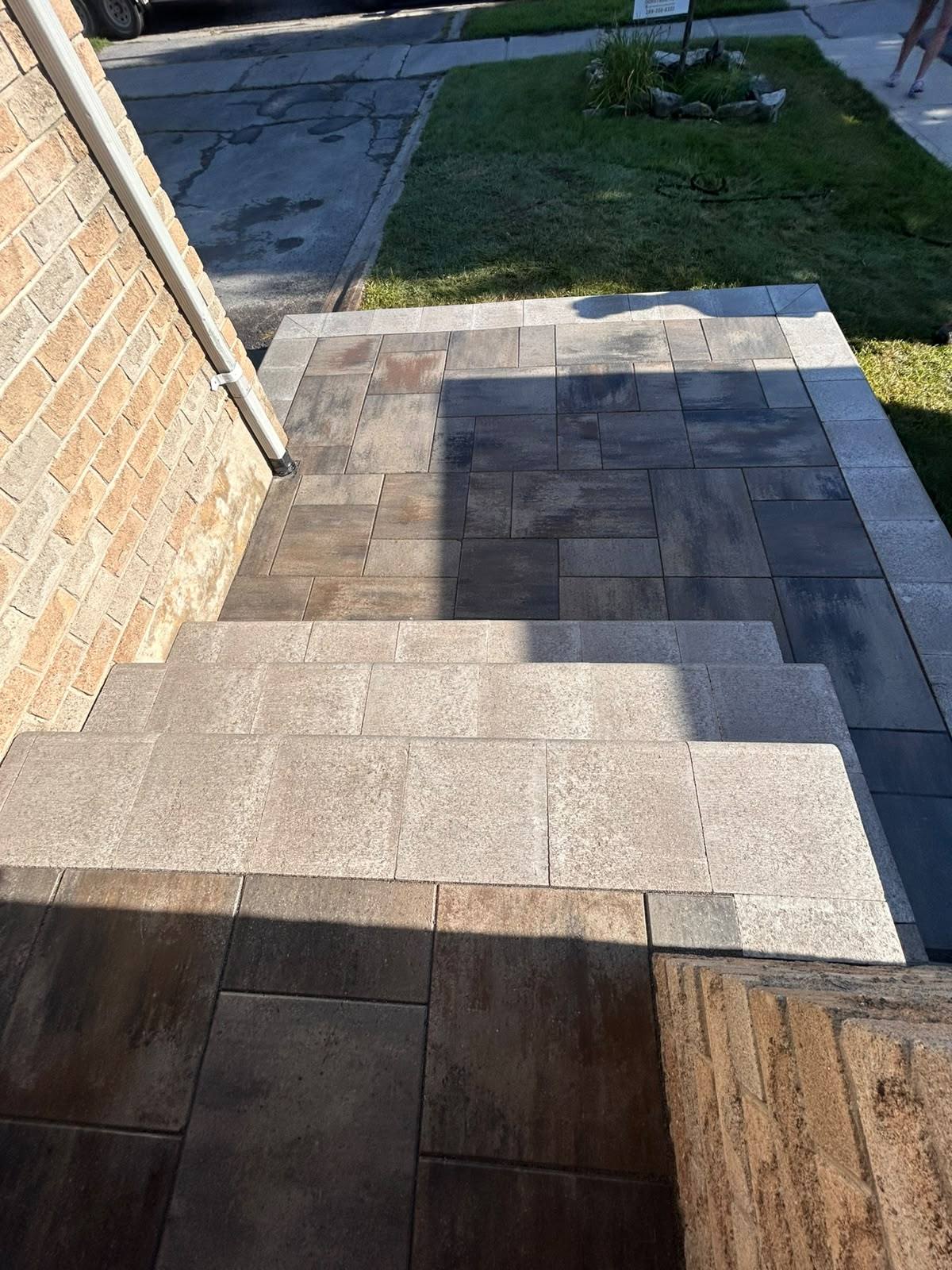 Overhead view of a grey large-format interlock entrance landing with a light border and charcoal accent band in Kingston, Ontario