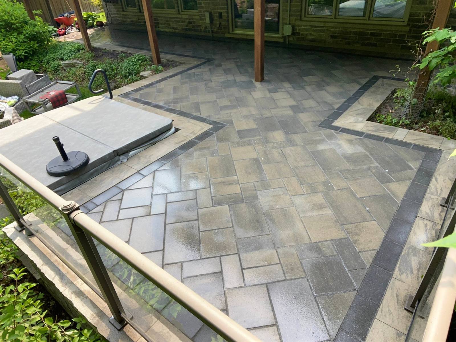 Interlock patio with banded border and glass railing around a hot tub, built by Gonzo Construction in the Kingston area