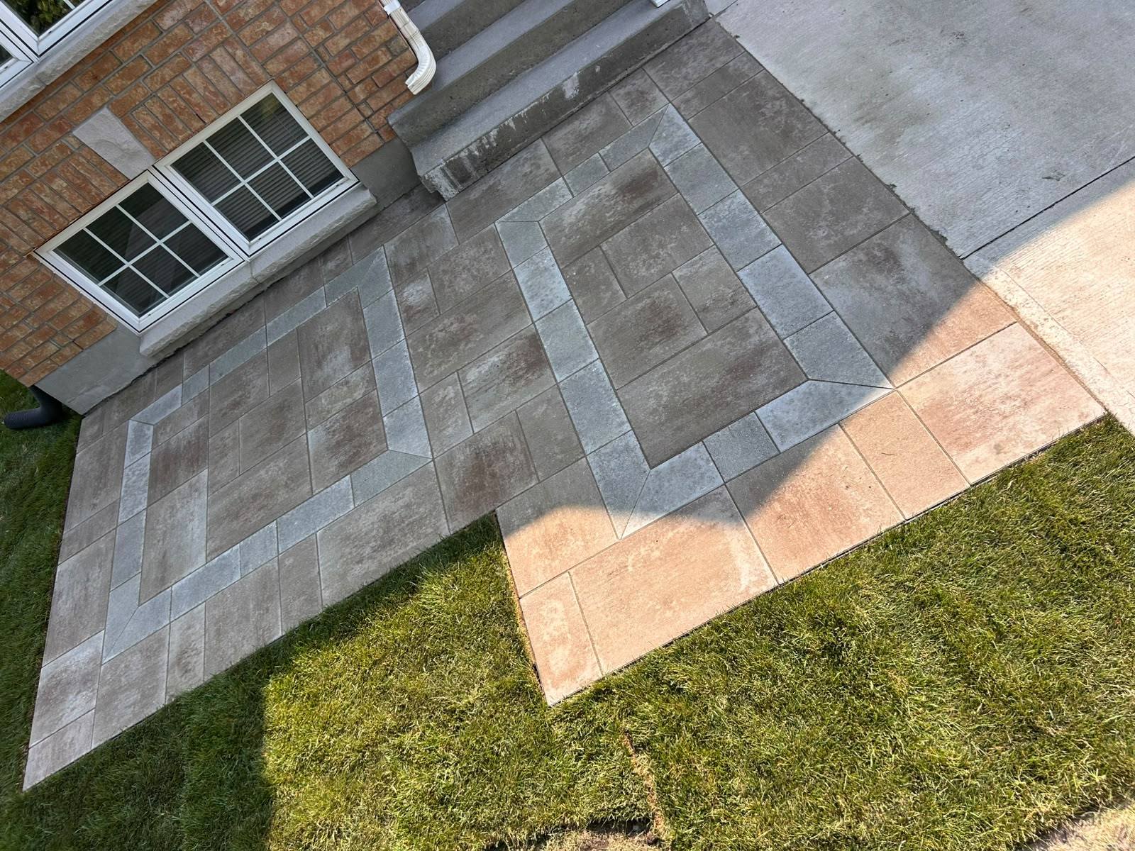 Overhead view of an interlock patio with a grey ashlar field and a tan bordered geometric inlay in Kingston, Ontario